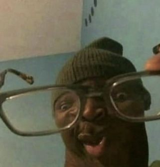 Um homem faz uma careta engraçada enquanto segura um par de óculos grandes bem próximo à câmera.